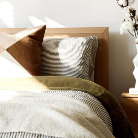 swath of sunlight shines across a well made bed and bedside table with a vase of cotton plants